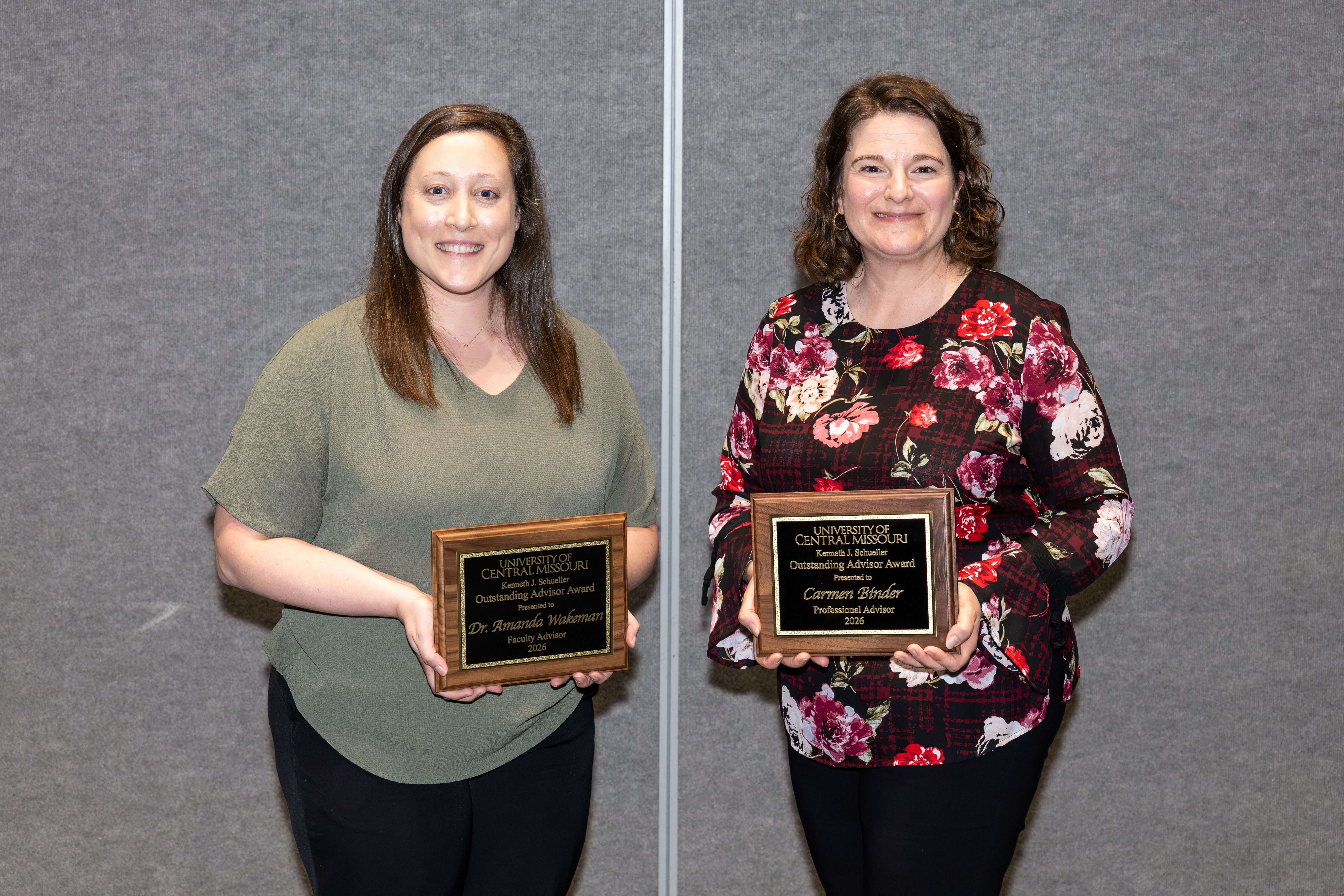 Two people stand next to each other while holding Outstanding Advisor Award plaques.