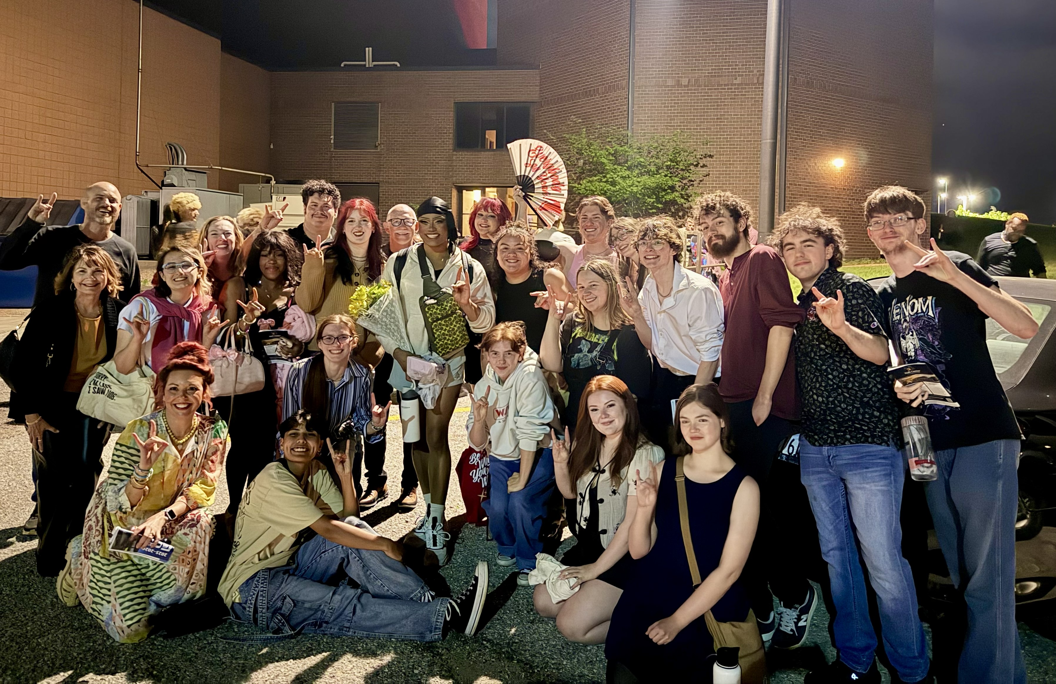 A group of more than 20 people are seen outside a building at night. Some are standing and some are kneeling. 