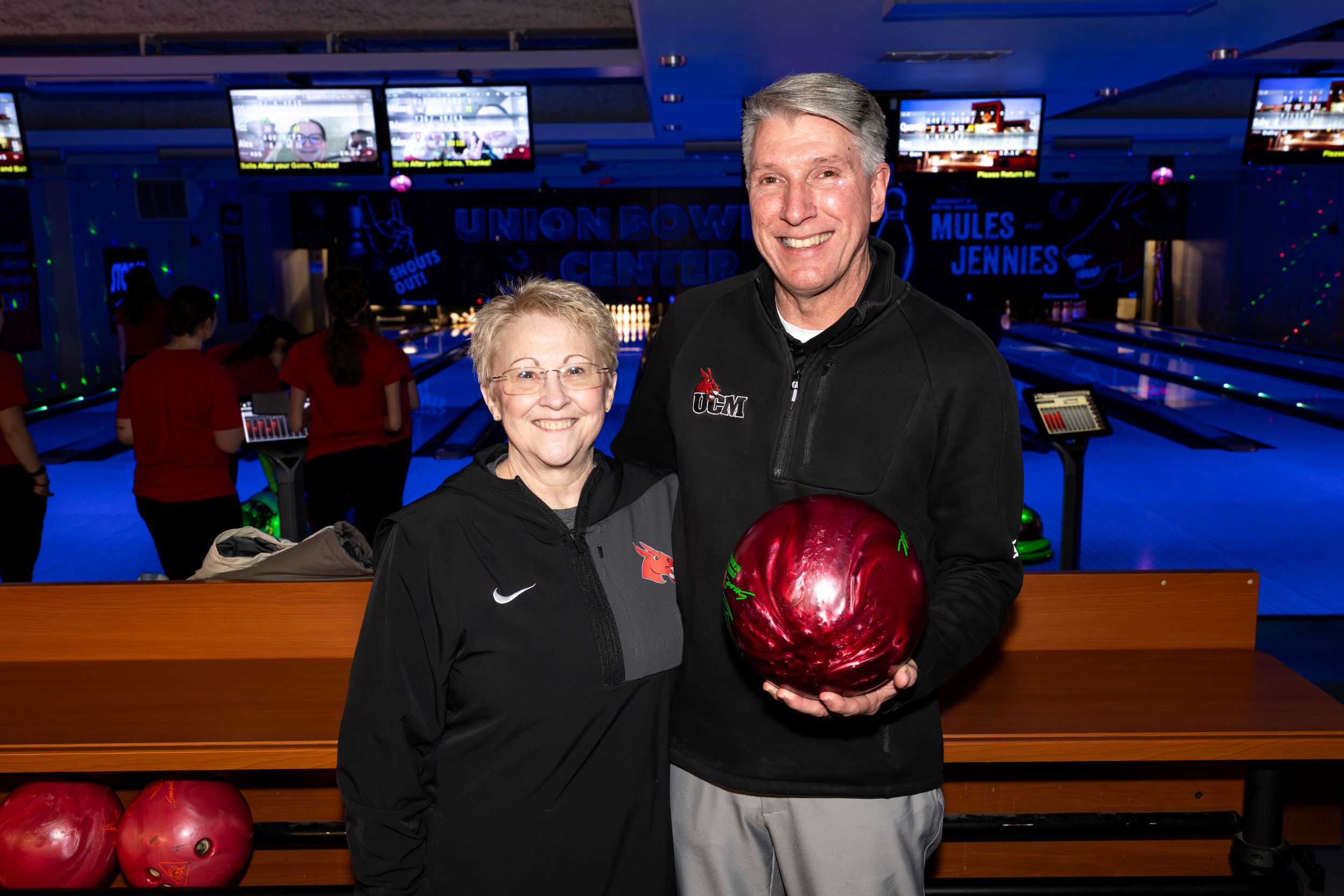 A man holding a bowling ball stands next to a woman in a bowling alley