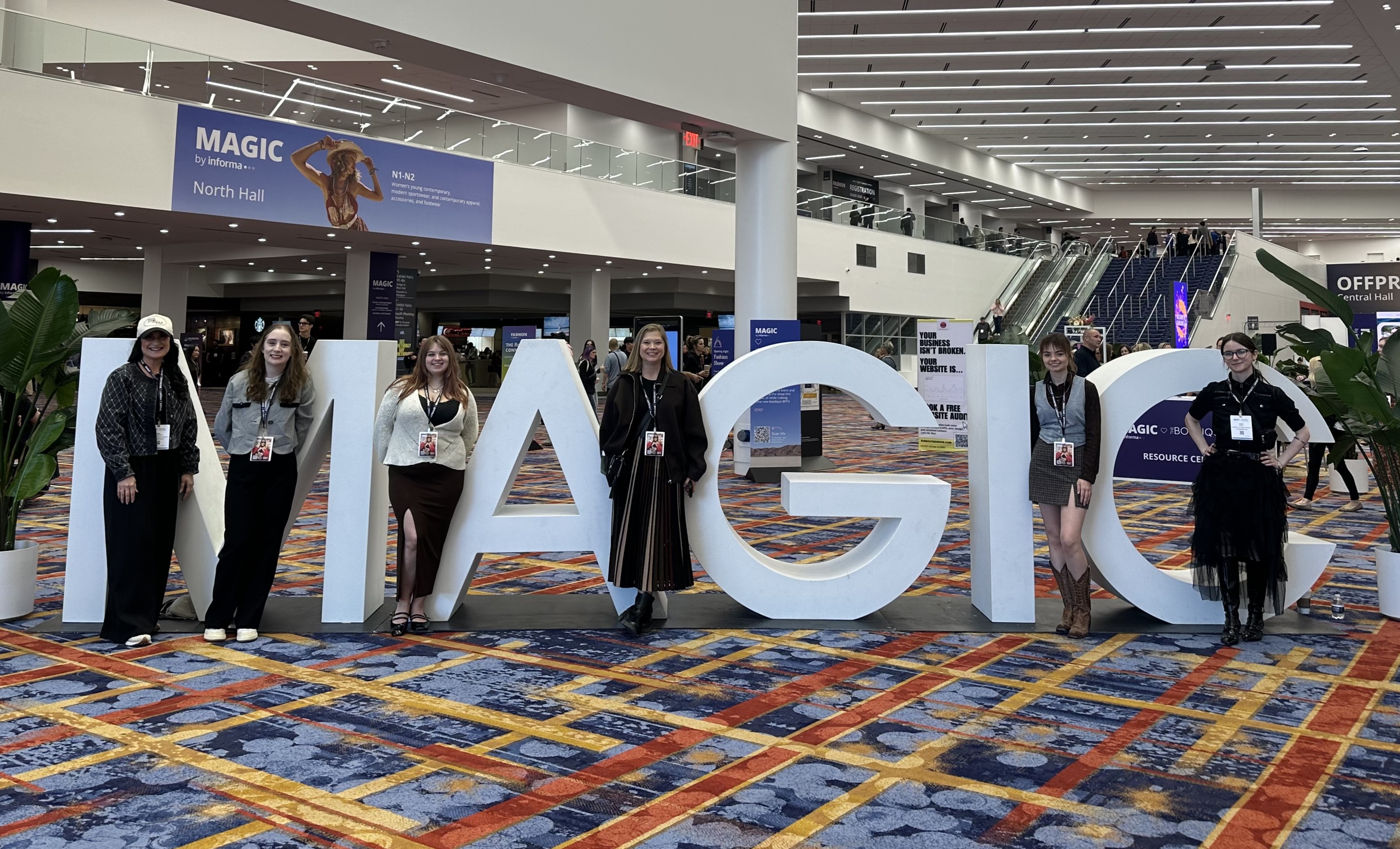 Six people stand in front of large white letters that spell MAGIC