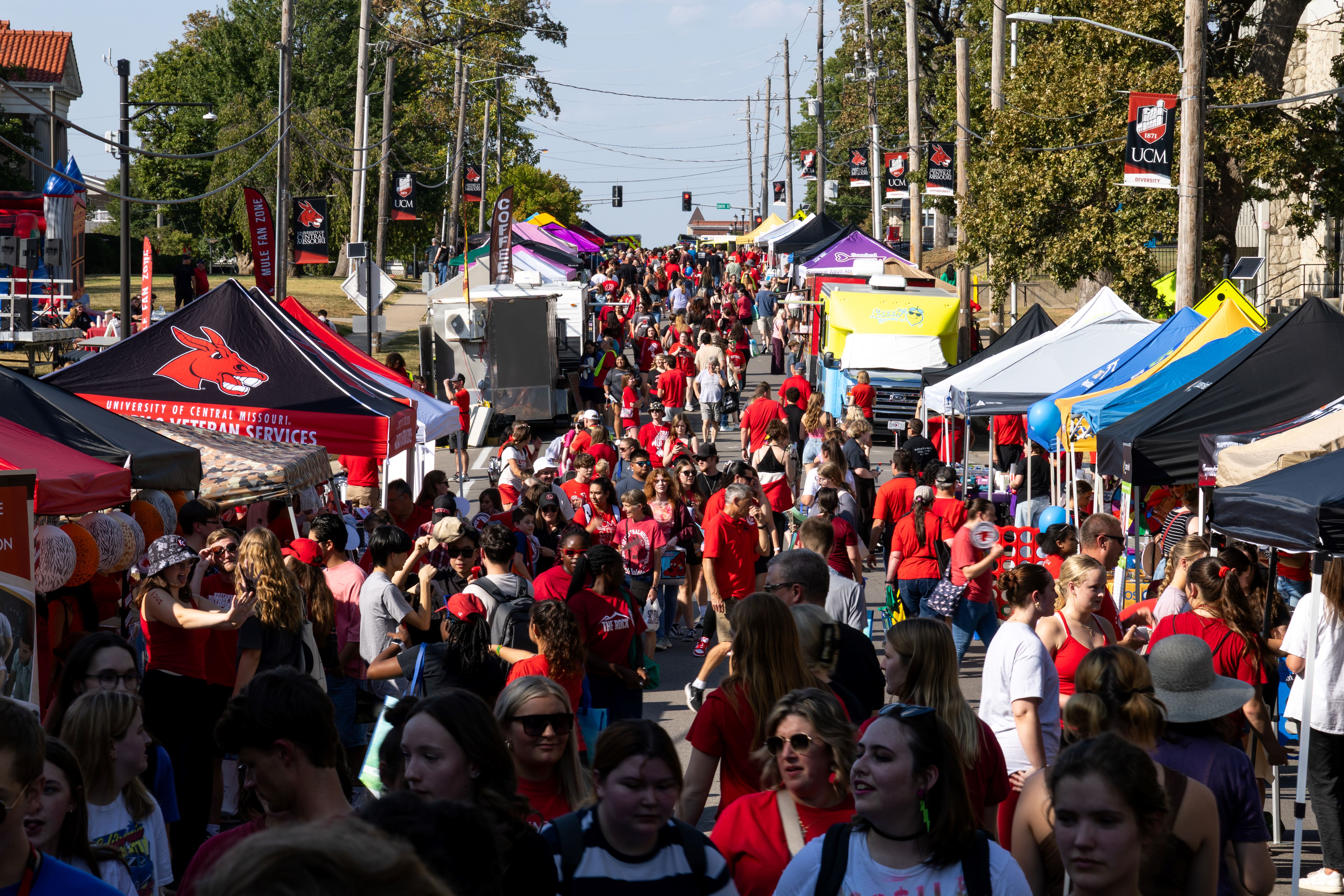 Get the Red Out South Holden Street is lined on either side with dozens of pop-up tents in various colors. Hundreds of people are seen in the street talking, looking at vendors and walking. The crowd stretches all the way down the street. It is a sunny day.