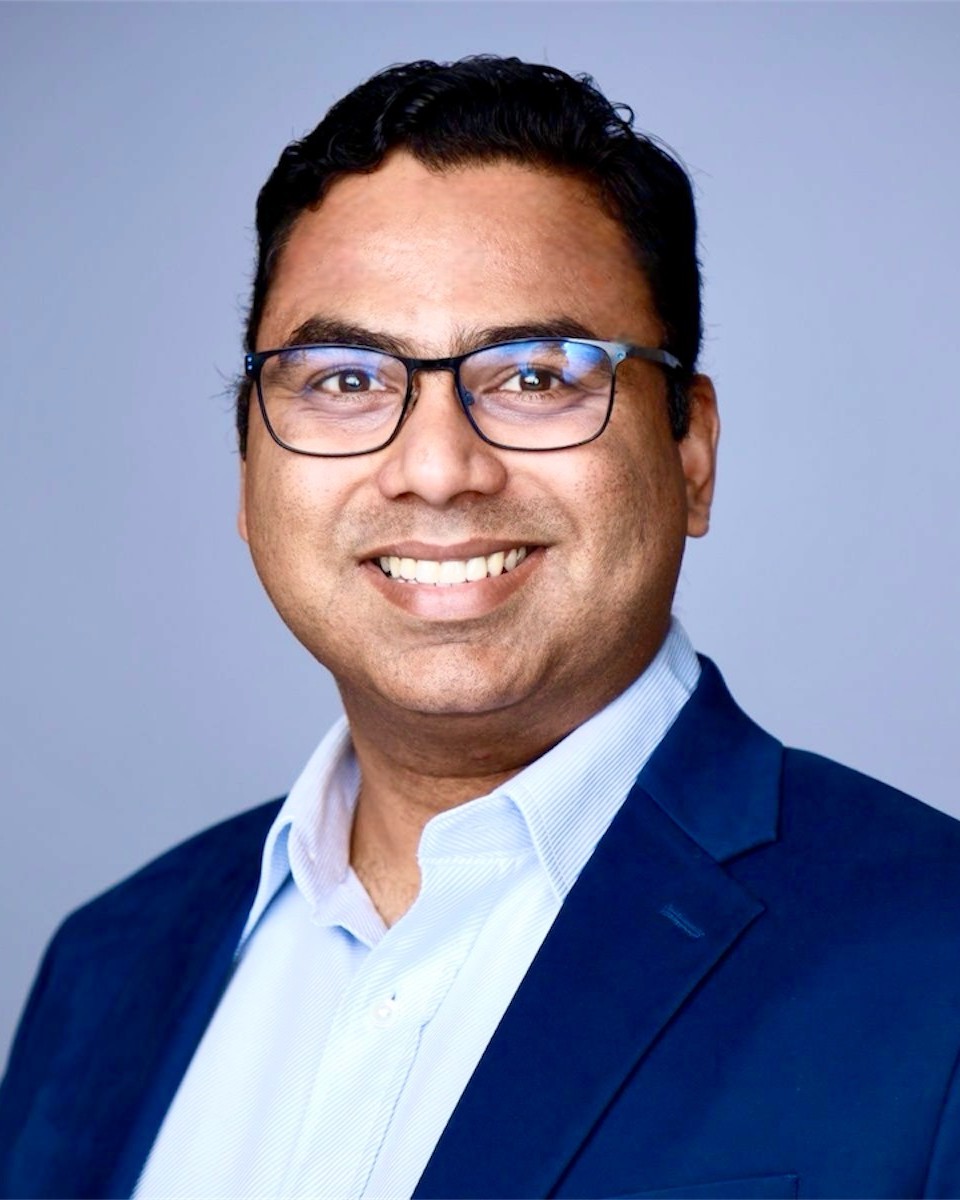 Abhi Shimpi Abhi Shimpi is seen in a professional portrait from the shoulders up. Abhi has short dark hair and is wearing black glasses, a white shirt and a dark blue suit jacket. The background is light blue.