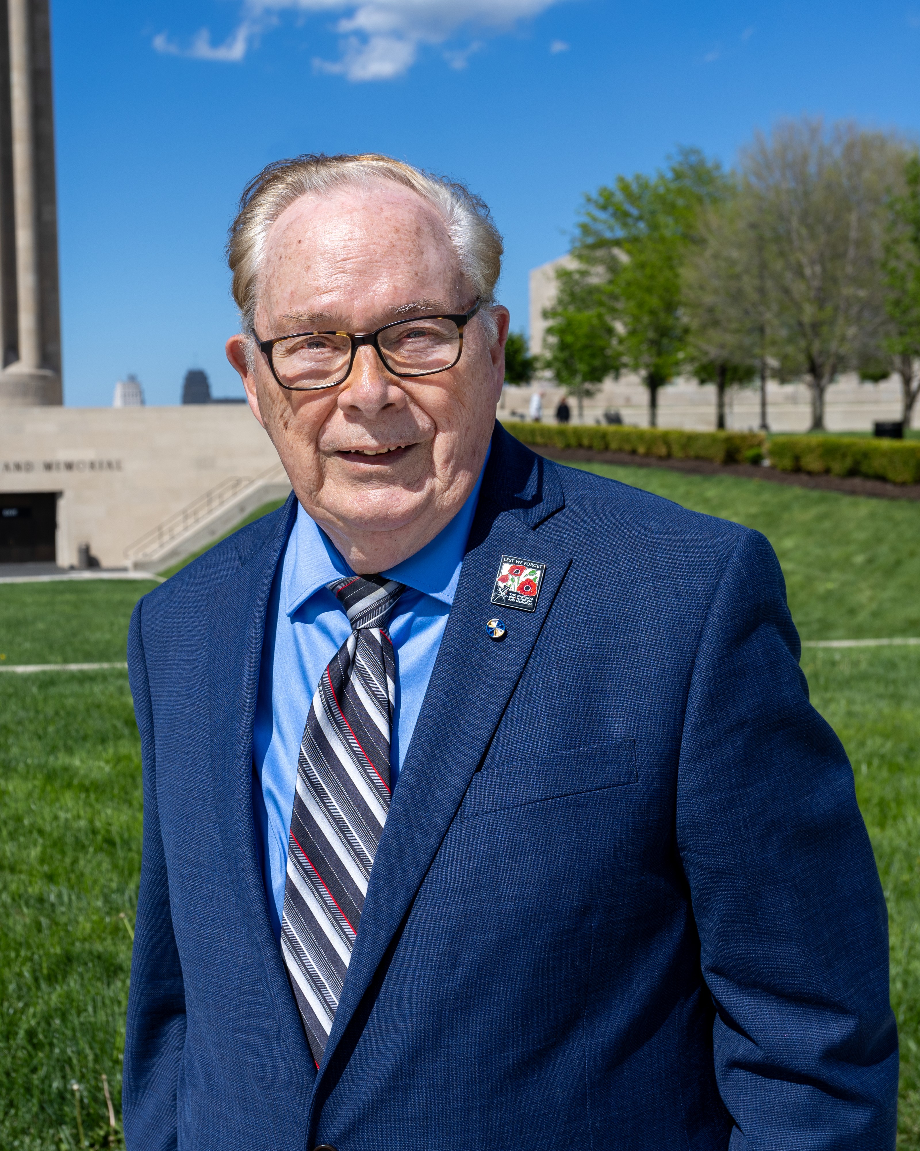 Kelton Smith Kelton Smith is seen in a professional portrait from the shoulders up. Kelton has short gray hair and is wearing dark brown glasses, a blue shirt, a gray-white-and-red tie and a dark blue suit jacket. He is outside, with bright green grass and trees behind him, along with part of the World War I Memorial stone tower.