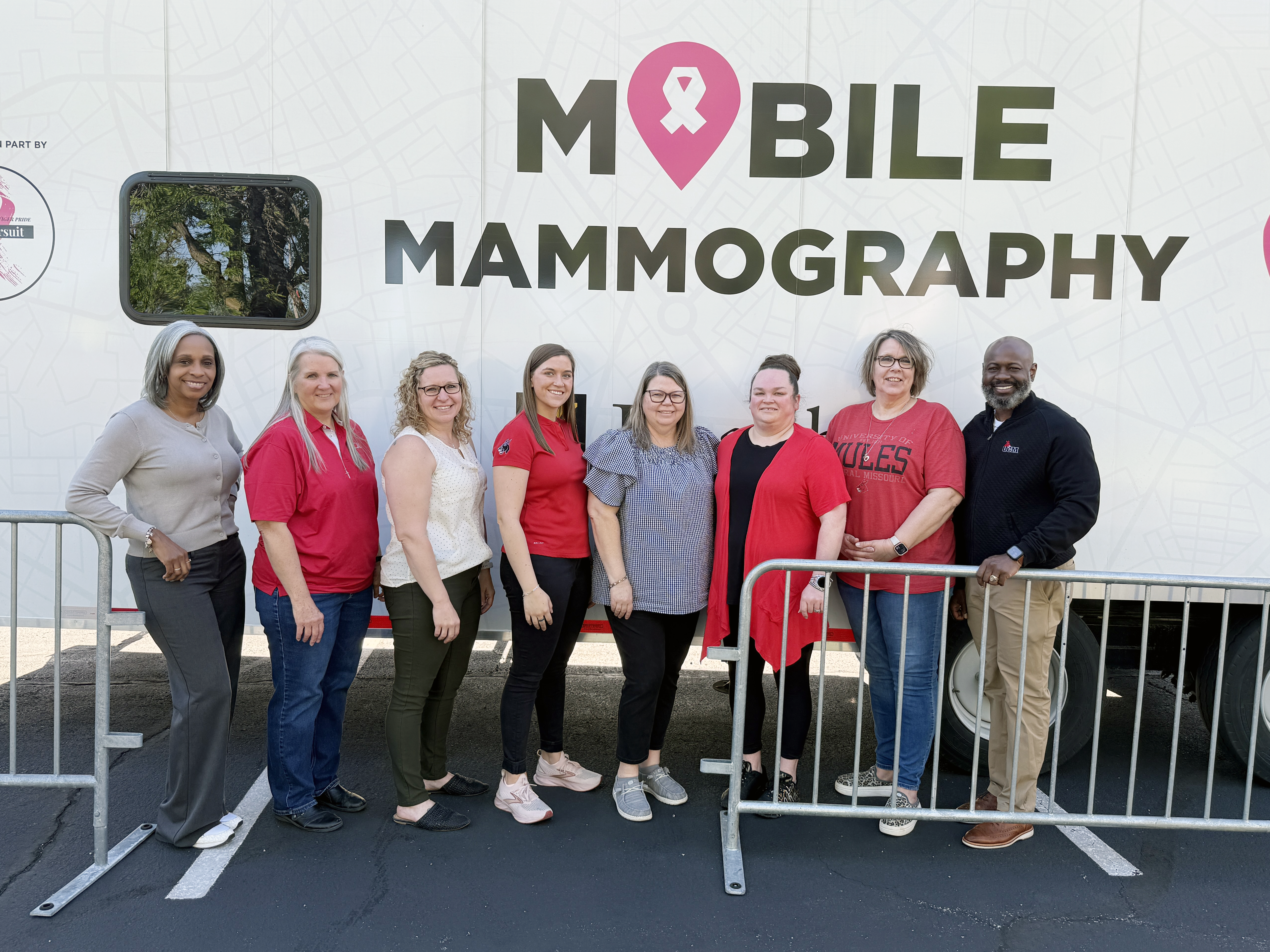 Eight people stand side by side in front of a white trailer that has 