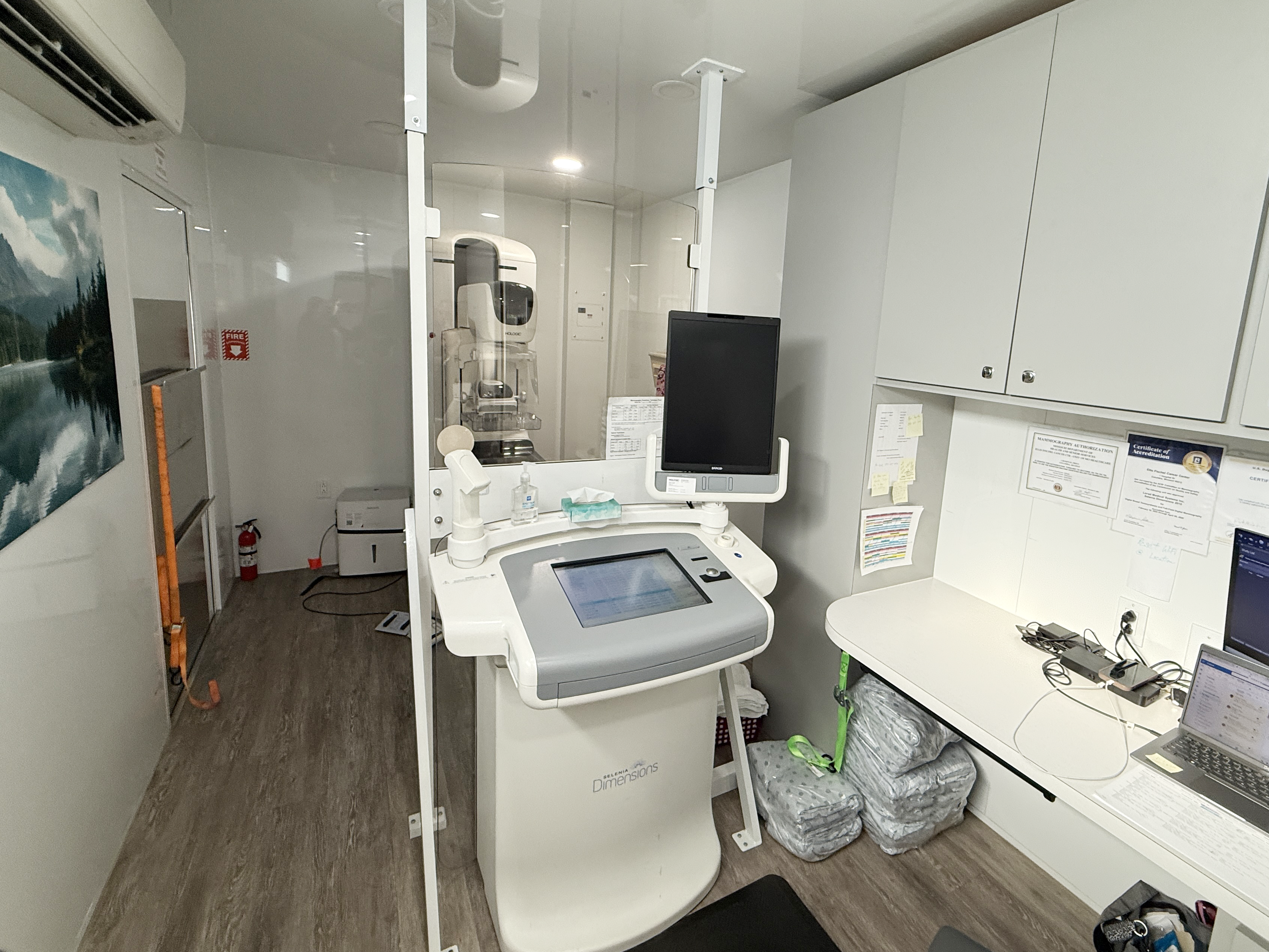 The inside of the mobile mammography unit is seen, including a counter with a laptop and 3D mammography equipment.