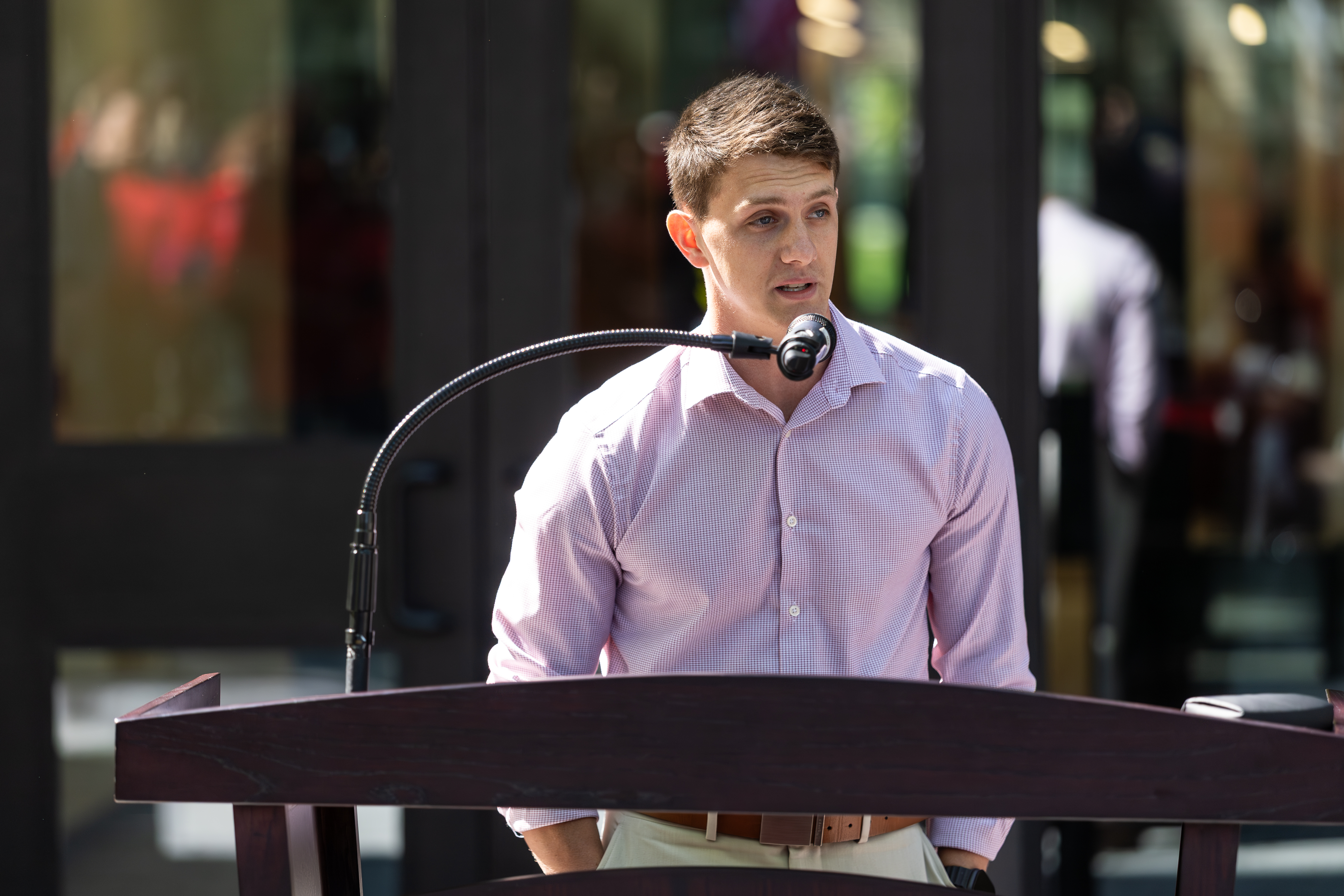 A young man stands behind a podium and speaks into a microphone.