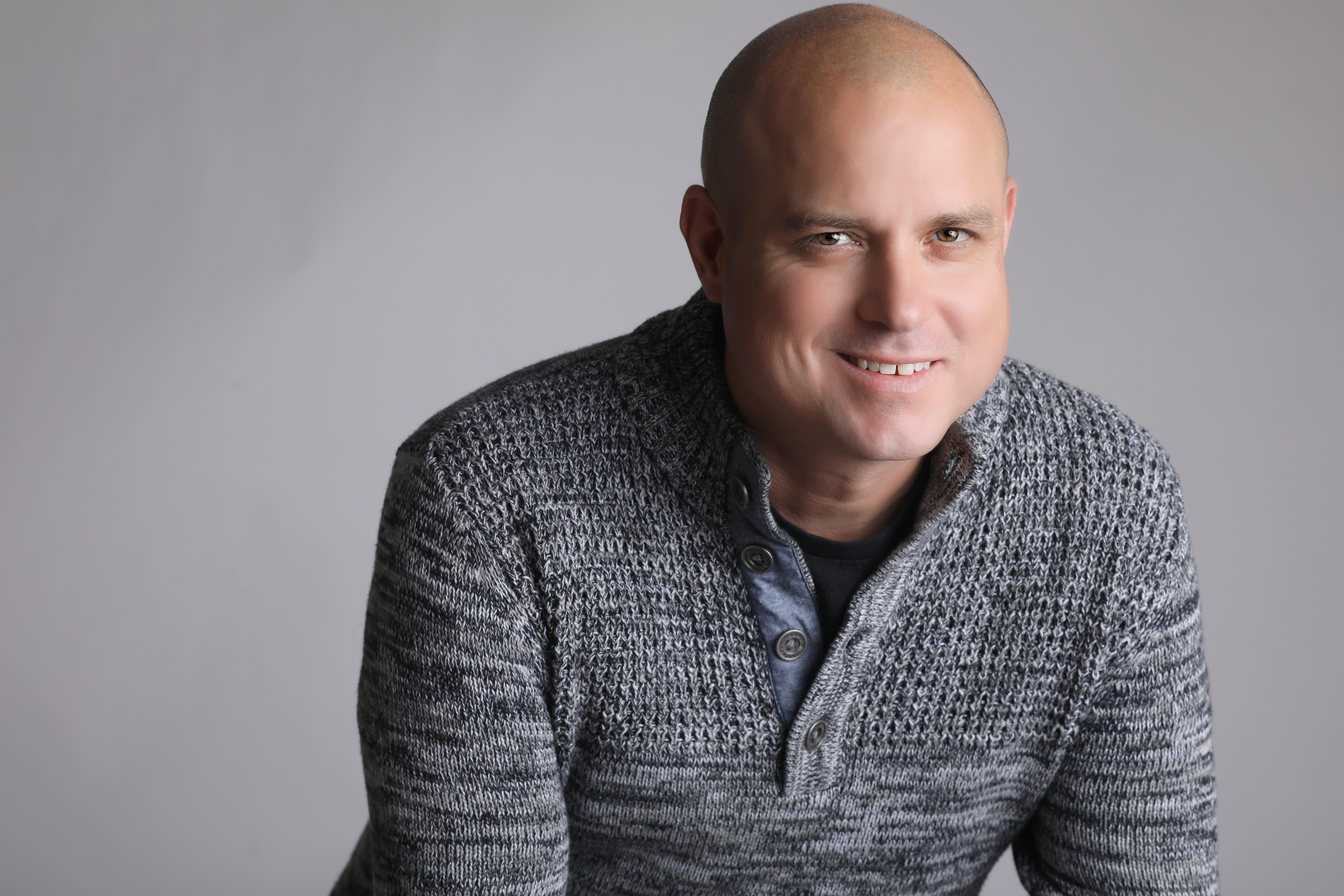 Aaron Scully A person is seen in a professional portrait wearing a gray sweater.