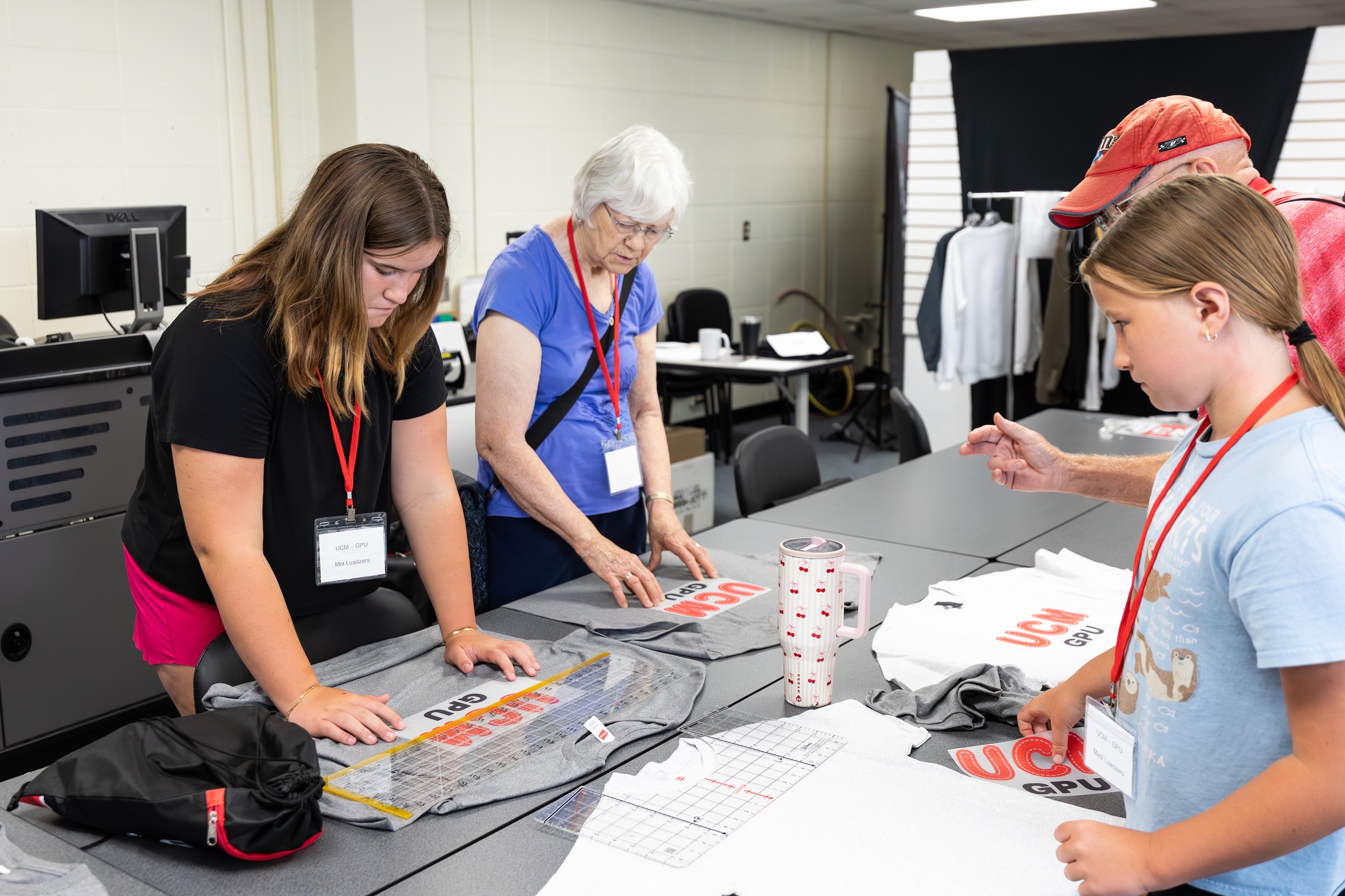 Grandparents University Two young students and two grandparents are measuring logos and shirts before adhering the UCM GPU logo.