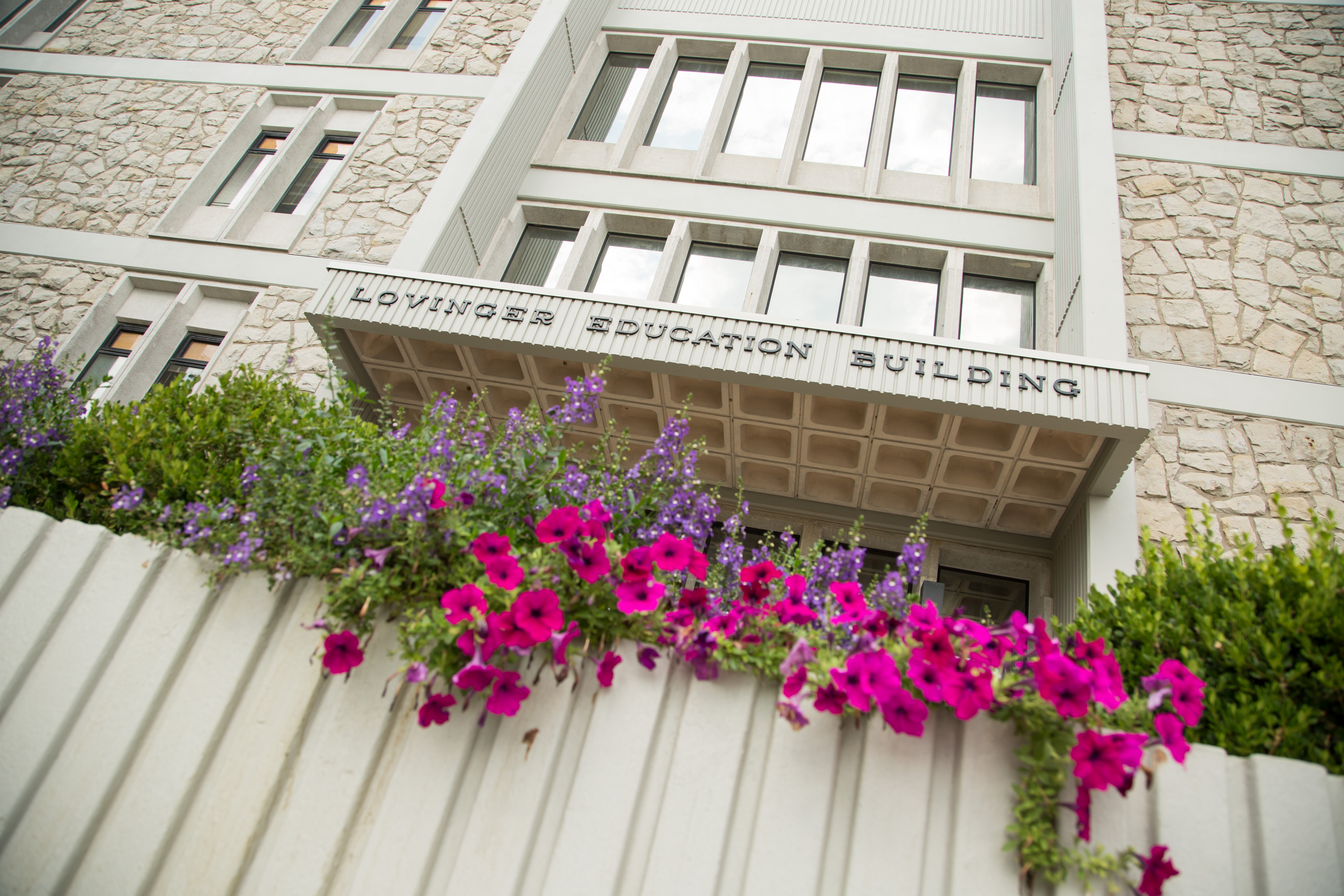 Lovinger Building A building with the words "Lovinger Education Building" across the entrance is seen. Brightly-colored purple flowers and green bushes are in front of the building.