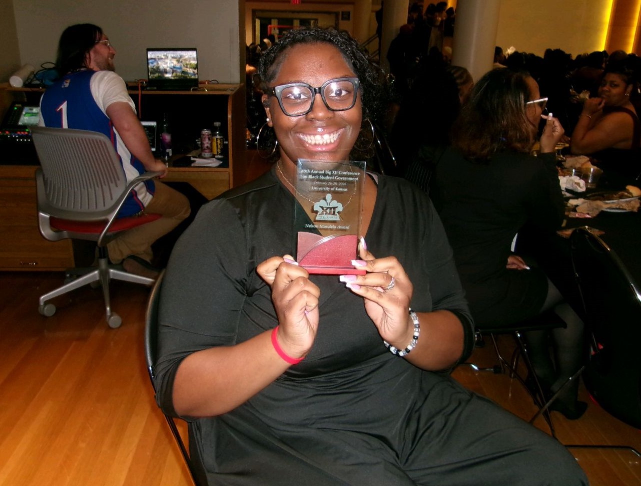 A person sitting in a chair is smiling and holding an award plaque.