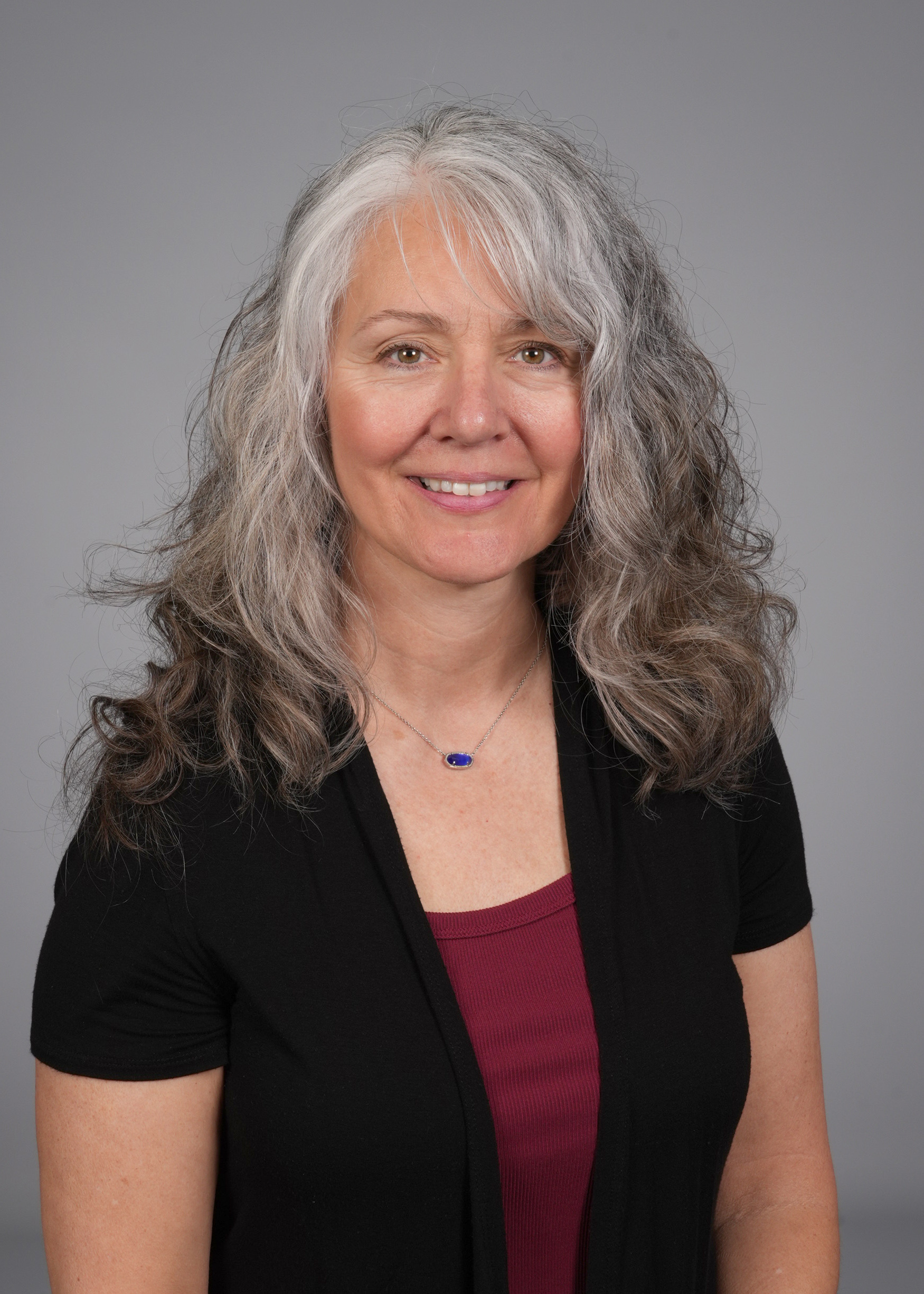 A person is seen from the shoulders up with a gray background. They are smiling.