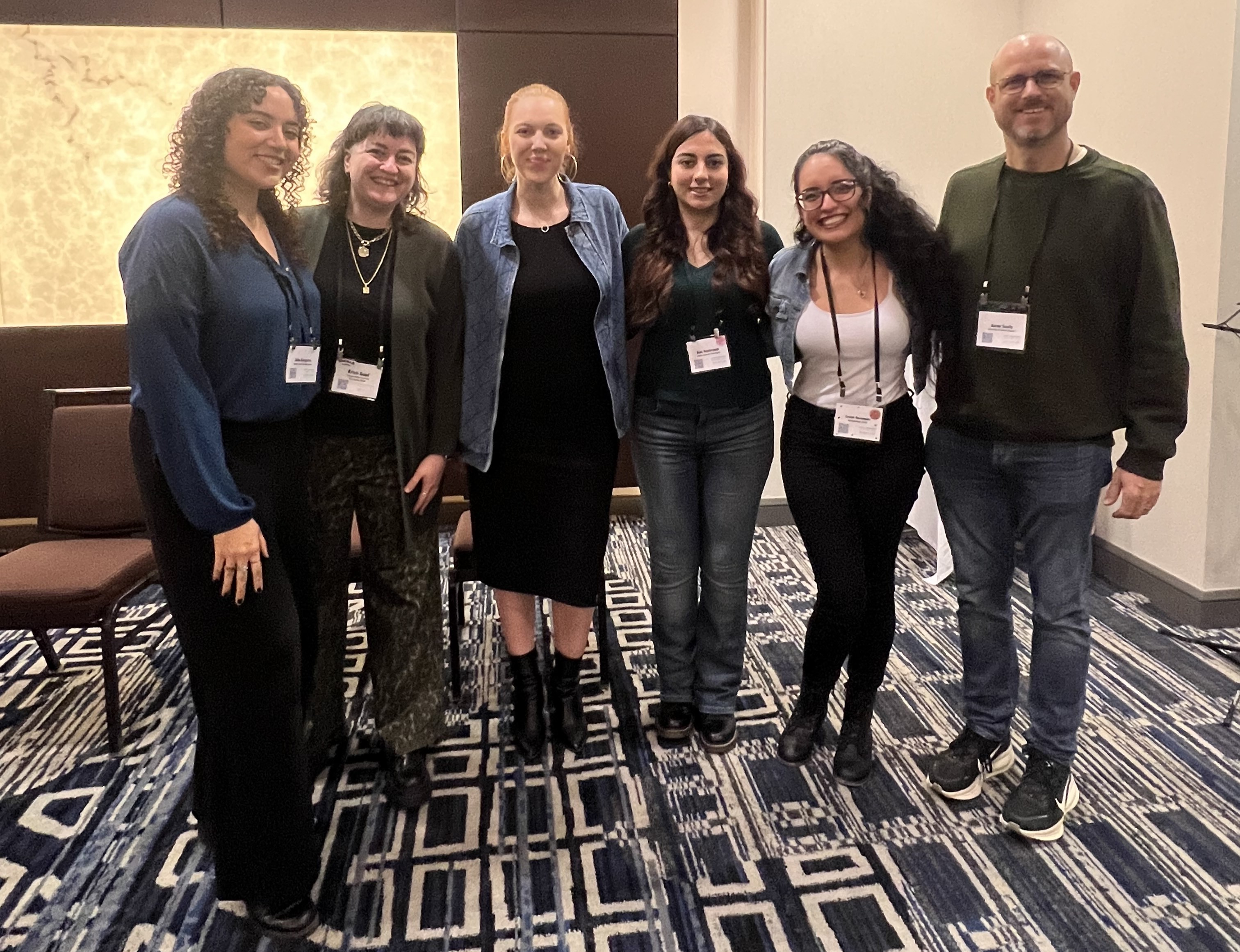 A group of people stands side by side while smiling inside a conference room.