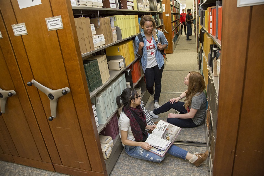 photo of three female studetns in the library book stacks
