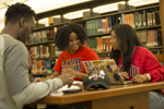 three students sitting at desk in library