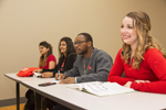 four students sitting at a row of desks in a classroom